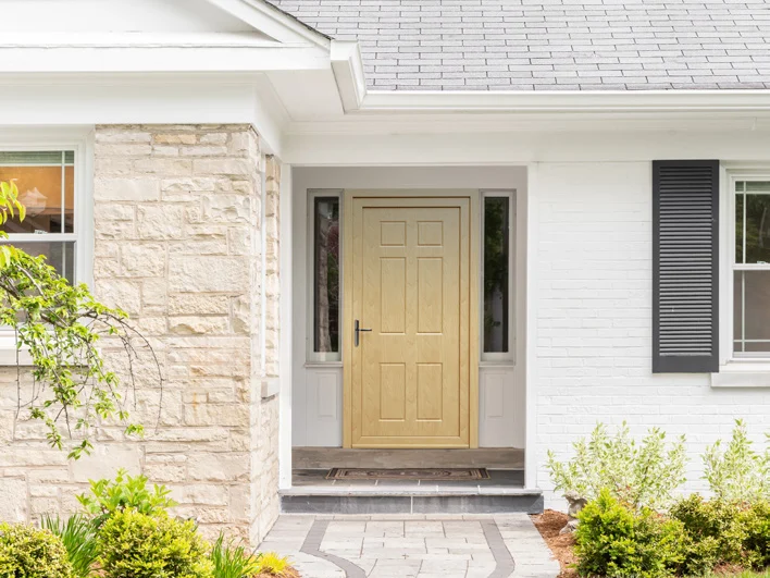 Porte d'entrée PVC aspect chêne avec fixes latéraux, maison en pierre claire